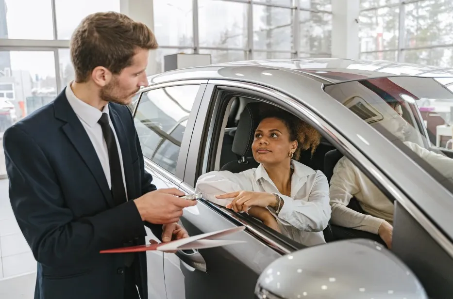 A car salesperson handing keys to a customer inside a new car, depicting the point of sale where Lemon Law protections begin.