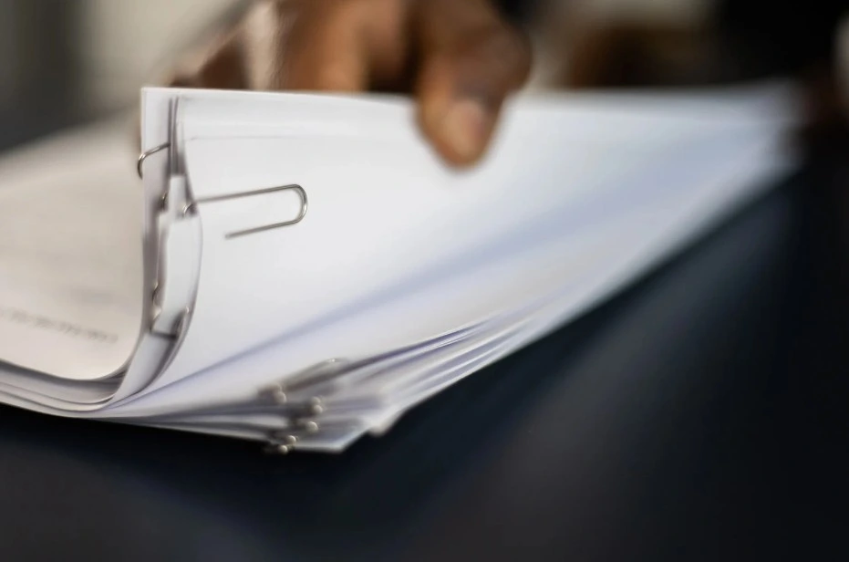 A hand flipping through a stack of documents secured with paperclips, symbolizing the paperwork and legal processes involved in a Lemon Law claim.
