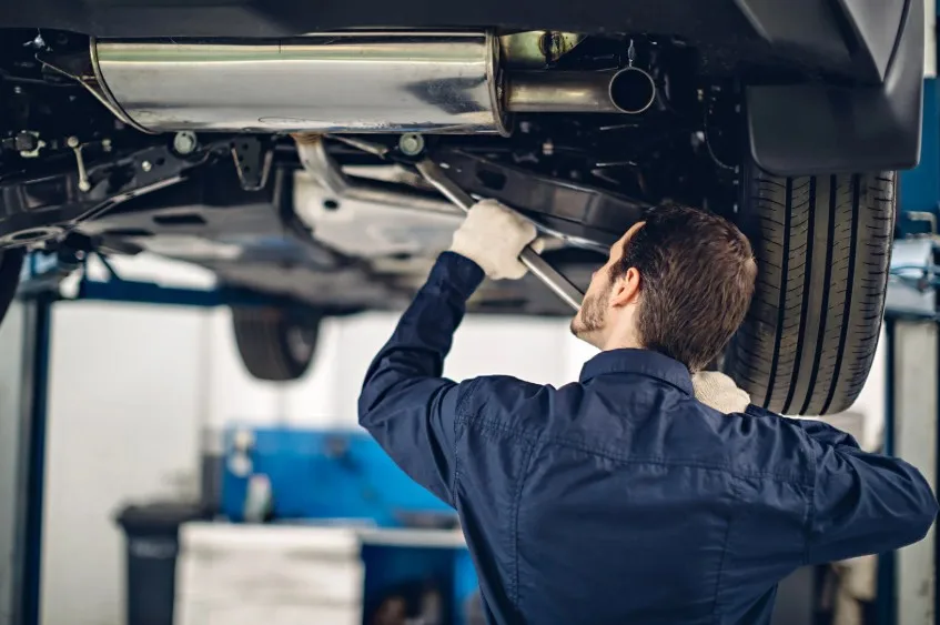 Mechanic inspecting undercarriage and exhaust system to diagnose recurring 2022 Ram 1500 problems at repair shop