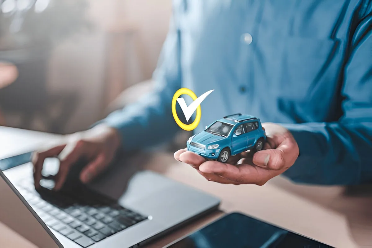 Person holding a model car with a verification checkmark while researching online what voids a car warranty