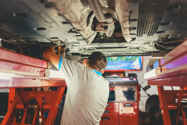 Auto mechanic inspecting car undercarriage on lift in repair shop