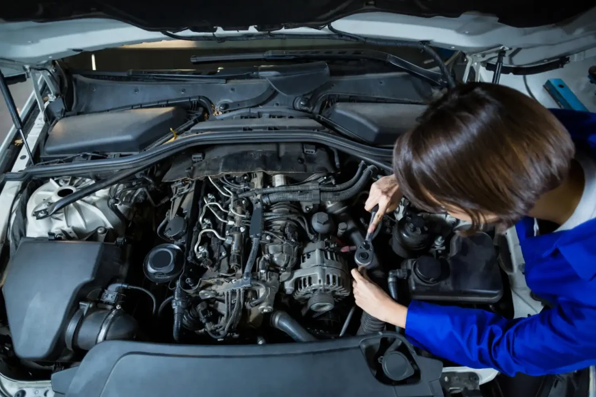 Female mechanic inspecting engine components under the hood to diagnose symptoms of a bad PCM causing performance issues