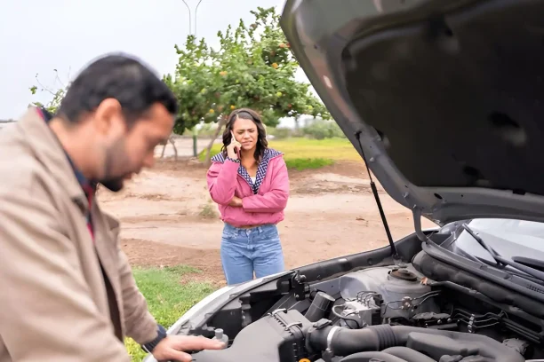 Woman calling for help while man checks broken car engine on roadside.