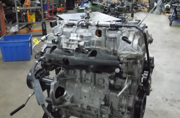 A mechanic holding and inspecting a car engine block inside an auto repair shop.