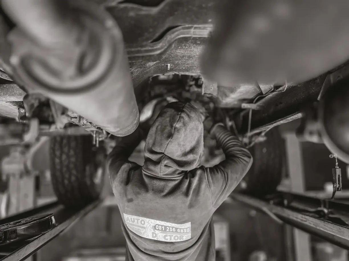 Auto mechanic inspecting and repairing vehicle components underneath a raised car