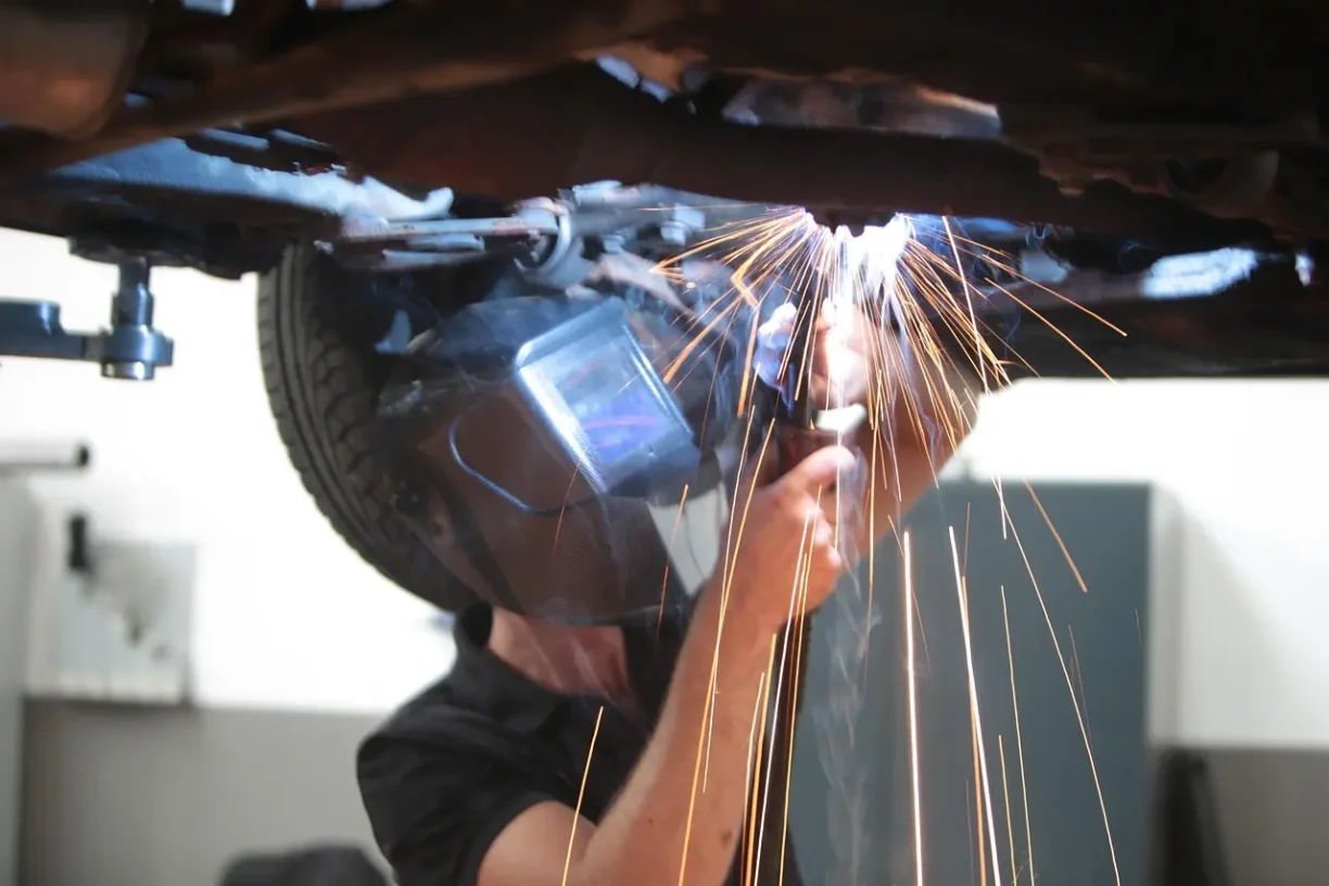 Auto mechanic welding and repairing the underside of a vehicle in a workshop