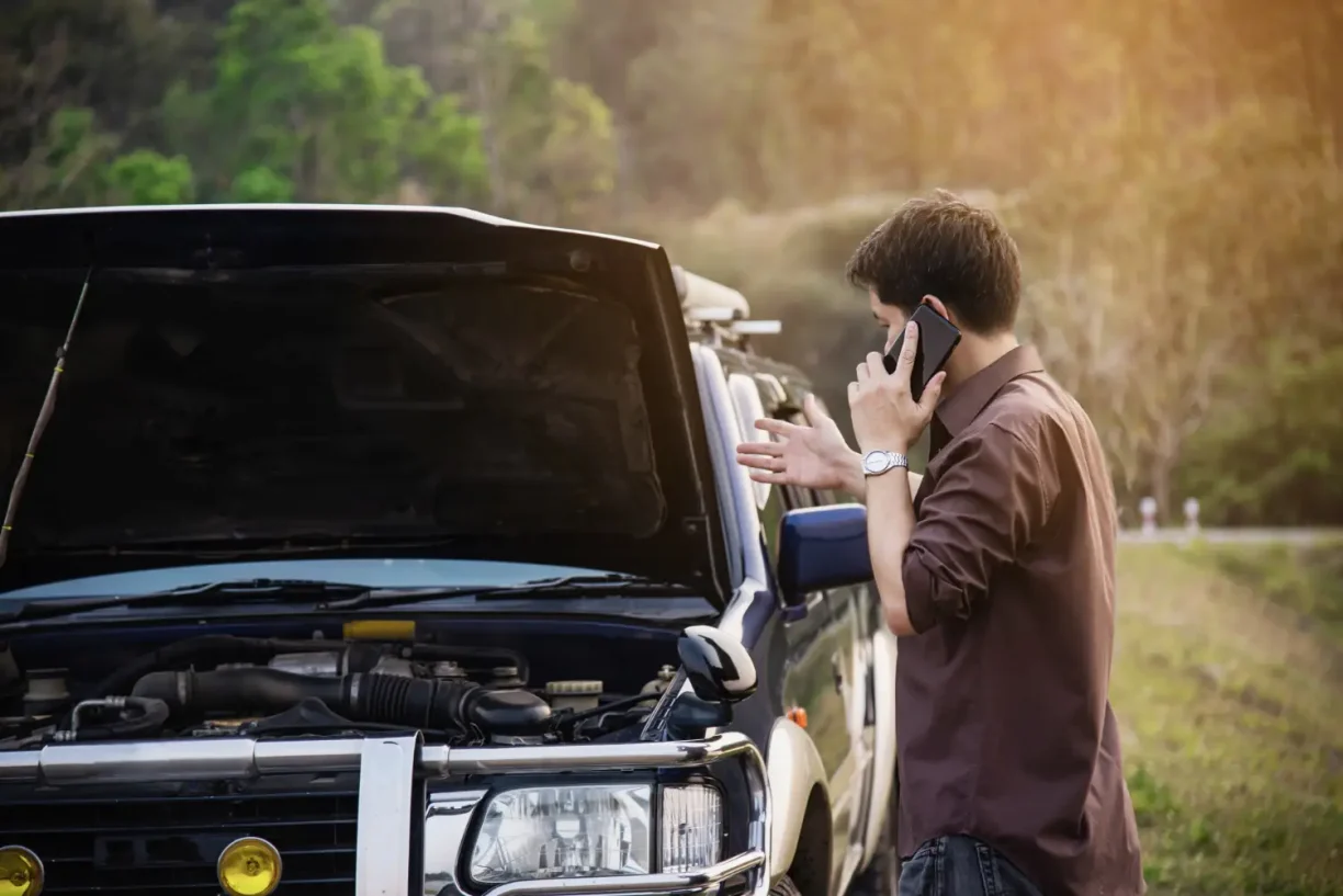 Driver standing beside broken down car while calling for roadside assistance