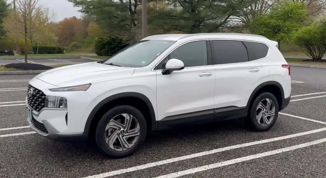 White midsize SUV parked outdoors, showing modern body design and side profile, commonly associated with recent Hyundai Santa Fe models.
