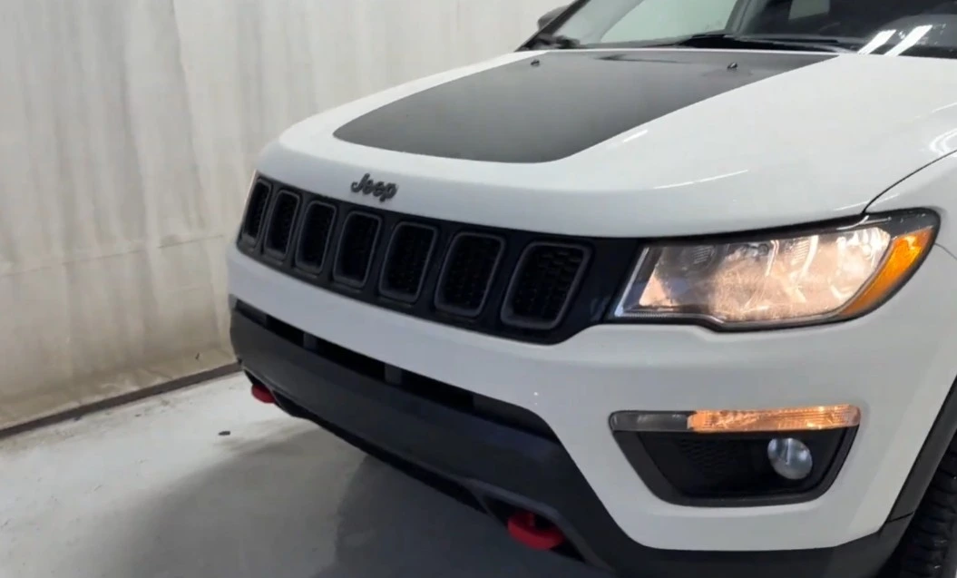 Front view of a white 2021 Jeep Compass Trailhawk with signature red tow hooks, a model often cited in consumer defect and lemon law cases.